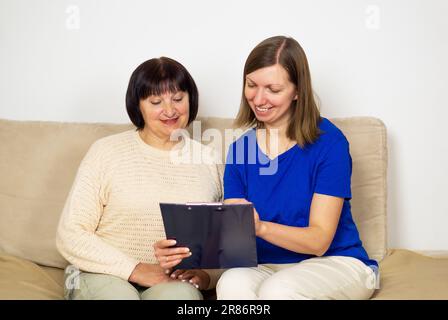 Giovane caregiver che mostra una precrizione o un documento e aiuta la donna anziana a casa. Foto Stock
