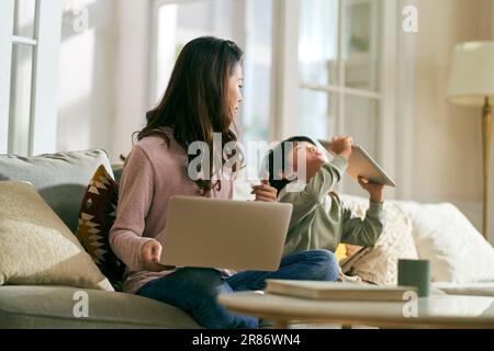 giovane madre asiatica d'affari cercando di lavorare a casa infastidita da figlio iperattivo Foto Stock