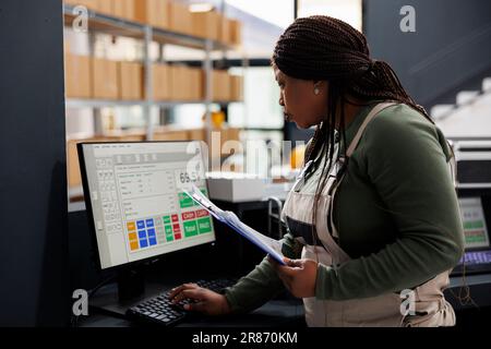 Operaio afroamericano che guarda il rapporto di inventario sul calcolatore, che lavora al controllo di qualità della merce in deposito. Supervisore magazzino che prepara gli ordini dei clienti per la spedizione in magazzino Foto Stock