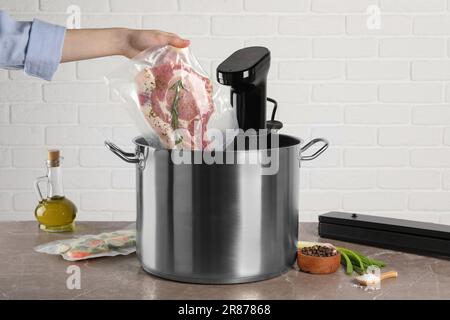 Donna che mette la carne sottovuoto impaccata in pentola con cucina sous vide, primo piano. Circolatore a immersione termica Foto Stock