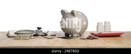 Banco di piggy, stetoscopio, calcolatrice e pillole su tavolo di legno su sfondo bianco. Assicurazione medica Foto Stock