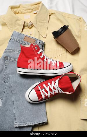 Paio di eleganti scarpe rosse, abiti e tazzina di carta su tessuto bianco, piatto Foto Stock