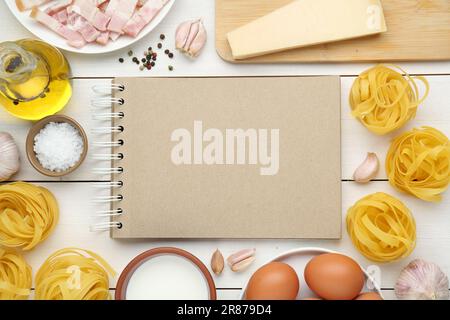 Libro di ricette in bianco circondato da diversi ingredienti su tavolo di legno bianco, piatto. Spazio per il testo Foto Stock