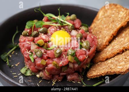 Gustose tartare di bistecca di manzo servite con tuorlo, capperi e pane in padella, primo piano Foto Stock