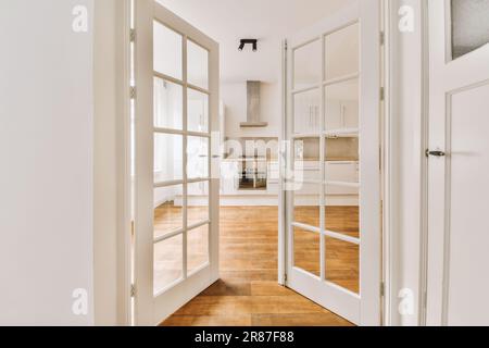 una stanza vuota con pareti bianche e pavimento in legno, come visto dalla porta alla zona cucina nella porta è aperta Foto Stock