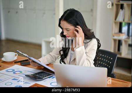 Una donna d'affari asiatica professionale e premurosa che legge e rivede i rapporti aziendali alla sua scrivania in ufficio. Foto Stock