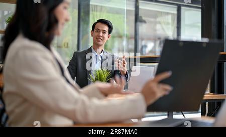 Un uomo d'affari asiatico, amichevole e intelligente, sta parlando e discutendo del lavoro con una collega in ufficio. lavoro di squadra, collaborazione, colleghi Foto Stock