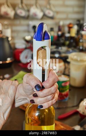 Donna apre una bottiglia di vino bianco con un cavatappi speciale Foto Stock