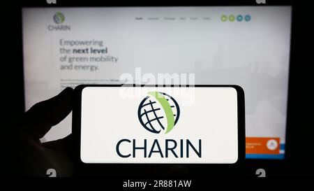 Persona che possiede uno smartphone con il logo dell'associazione globale di tariffazione Charin e.V. sullo schermo davanti al sito Web. Concentrarsi sul display del telefono. Foto Stock