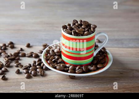 Chicchi di caffè in tazza a righe su un tavolo di legno Foto Stock