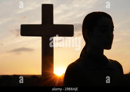 Ateismo. Silhouette di donna si allontanò dalla croce cristiana all'aperto all'alba Foto Stock