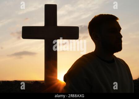 Ateismo. Silhouette dell'uomo si allontanò dalla croce cristiana all'aperto all'alba Foto Stock