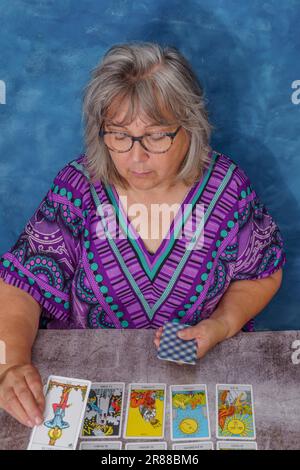 Donna più anziana con capelli bianchi e bicchieri che gettano le carte tarocchi Foto Stock