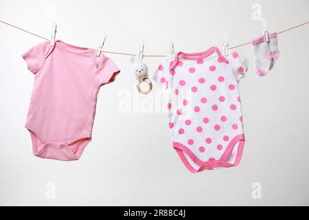 Cute baby onesies, calzini e uncinetto giocattolo asciugando sulla linea di lavaggio su sfondo bianco Foto Stock