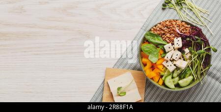 Delizioso recipiente vegano con peperone, tofu e grano saraceno su tavolo di legno, vista dall'alto. Design banner con spazio per il testo Foto Stock