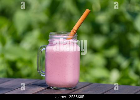 Frullato fresco di fragole refrigerate in una tazza di vetro su un tavolo di legno in una giornata di sole estate, primo piano. Rinfrescante bevanda di frutta estiva. Il concetto di guarire Foto Stock