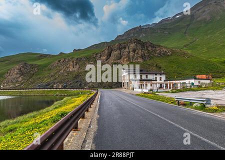 Casa abbandonata e piccolo lago alpino lungo la strada in montagna sotto il cielo nuvoloso e tempestoso vicino al Colle della Maddalena in Italia. Foto Stock