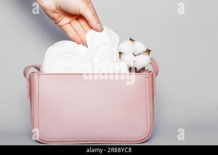 La mano da donna toglie il rivestimento della mutandina dalla borsa cosmetica rosa con tamponi e tamponi igienici femminili. Foto Stock