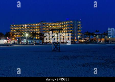 Questa immagine raffigura una scena fronte spiaggia con più edifici illuminati lungo la costa e un edificio più grande in lontananza Foto Stock