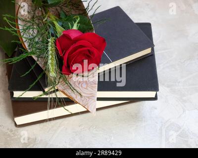 Una luminosa rosa rossa riposa su una pila di libri su uno sfondo bianco Foto Stock