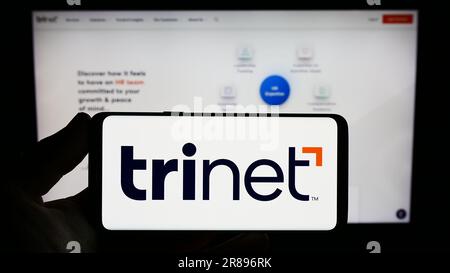 Persona che possiede uno smartphone con il logo della società di outsourcing statunitense TriNet Group Inc. Sullo schermo davanti al sito Web. Concentrarsi sul display del telefono. Foto Stock