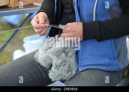 Mani di una donna che gira la lana grigia cruda in filo in un mercato artigianale in Germania, selezionato fuoco Foto Stock