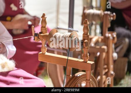 Ruota di legno che gira con una bobina rotante in movimento sfocata, artigianato tessile tradizionale da donna per fare fili lunghi da lana cruda, dimostrazione a a. Foto Stock