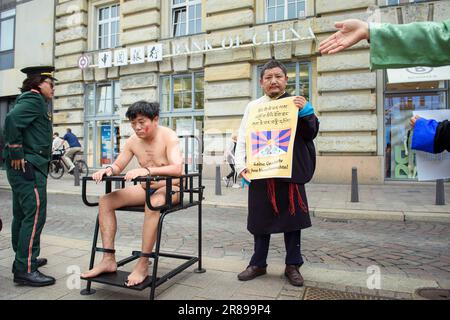 Amburgo, Germania. 20th giugno, 2023. Un attivista (2nd da sinistra) siede su un'imitazione di un presidente di tigre durante un'azione di protesta degli attori tibetani contro i crimini dei diritti umani in Tibet di fronte a un ramo della Banca della Cina presso il Rathausmarkt. Su una cosiddetta sedia della tigre, le persone sono immobilizzate durante l'interrogazione. Credit: Gregor Fischer/dpa/Alamy Live News Foto Stock