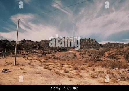 Un ambiente arido e desertico caratterizzato da linee elettriche e poli telefonici in cima al terreno. Perù. Foto Stock