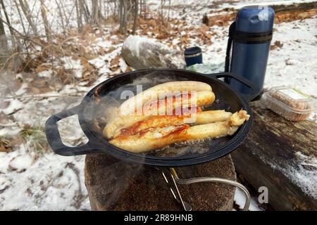 Salsicce in ciotola nella foresta in inverno. Camping alimentare. Cibi nelle attività all'aperto. Foto Stock