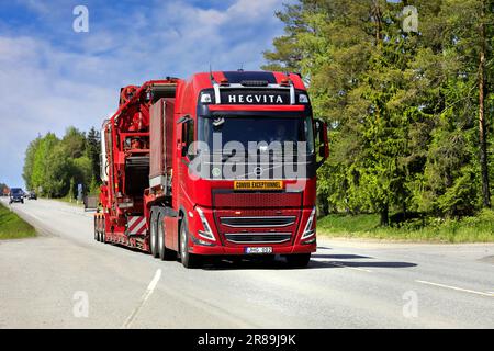 Il nuovo veicolo Volvo FH rosso Hedgvita trasporta i macchinari agricoli sul semirimorchio con caricatore basso come carico eccezionale. Jokioinen, Finlandia. Giugno 9, 2023. Foto Stock