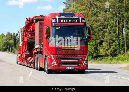 Il nuovo veicolo Volvo FH rosso Hedgvita trasporta i macchinari agricoli sul semirimorchio con caricatore basso come carico eccezionale. Jokioinen, Finlandia. Giugno 9, 2023. Foto Stock