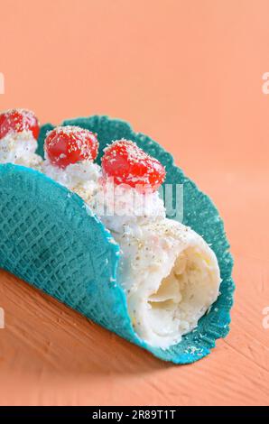 Rotolo di gelato di piña colada in cono cialde e ciliegie su sfondo arancione Foto Stock