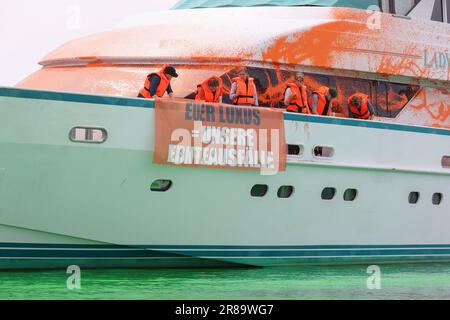 20 giugno 2023, Schleswig-Holstein, Neustadt in Holstein: Partecipanti a uno stand di protesta con striscioni su uno yacht nel porto di Neustadt. Su un banner c'è l'iscrizione 'il vostro lusso = i nostri crop fails'. Gli attivisti del gruppo Letzte Generation hanno spruzzato una barca con vernice a Neustadt in Holstein il martedì. Come parte dell'azione, anche l'acqua nel porticciolo era colorata di verde con una tintura. Foto: --/dpa Foto Stock