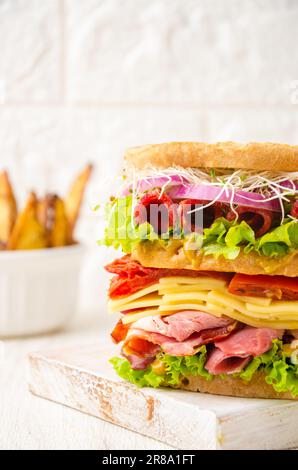 Club sandwich con patate rustiche. Pomodori, salsiccia, prosciutto, lattuga, formaggio giallo, germogli. Foto Stock