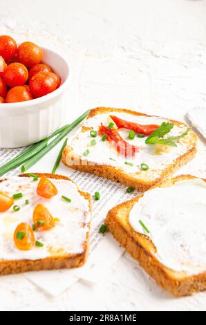 Fette di pane tostate con formaggio cremoso e pomodori ciliegini. Sfondo bianco. Foto Stock