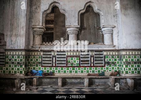 Gli uomini dormono nell'edificio dell'epoca coloniale presso il mercato dei Fiori di Mallick Ghat a Kolkata, in India Foto Stock