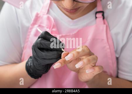 primo piano delle mani di una donna che rimuove i difetti dopo l'applicazione di smalto per unghie Foto Stock