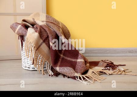 Cestino con nuova coperta morbida e schermo pieghevole vicino alla parete gialla in camera Foto Stock