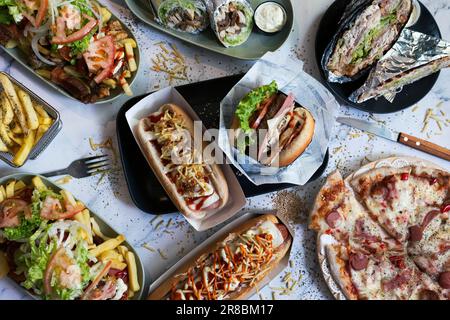 Varietà di piatti di cibo spazzatura sul tavolo. Hot dog, patatine fritte, salchipapas Foto Stock