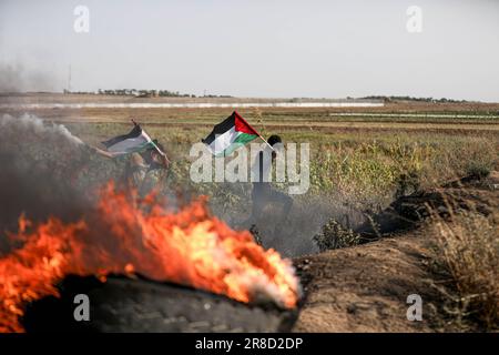 Un palestinese sventola una bandiera nazionale in mezzo a pneumatici bruciati vicino alla barriera di confine con Israele, a est di Gaza City, durante una protesta contro un raid militare israeliano su Jenin, in Cisgiordania. Foto Stock