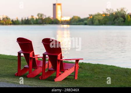 Sedie rosse Adirondack sulla riva del lago a Ottawa, Canada. Serena scena serale. Bellezza serena. Foto Stock