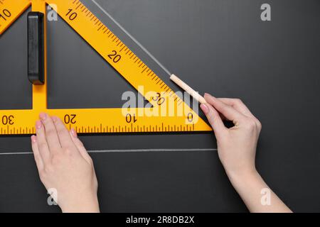 Donna che disegna con gesso e righello triangolare su lavagna, primo piano Foto Stock
