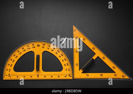 Goniometro, righello triangolare e gesso su tavola nera, giacitura piatta. Spazio per il testo Foto Stock