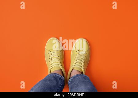 Donna in sneaker eleganti su sfondo arancione, vista dall'alto Foto Stock