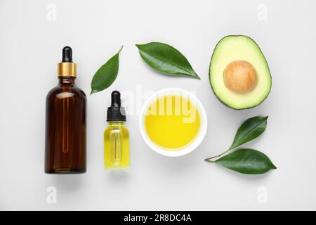 Olio essenziale, avocado fresco tagliato e foglie su fondo bianco, piatto Foto Stock