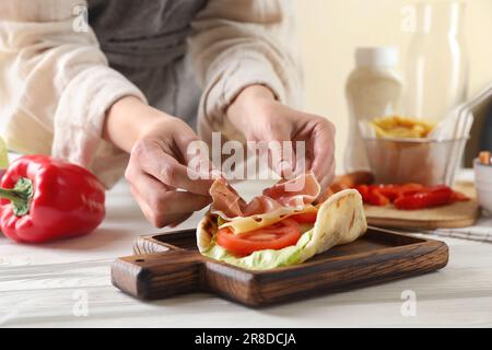 Donna che cucina delizioso pita wrap con jamon, formaggio e verdure a tavola di legno, primo piano Foto Stock