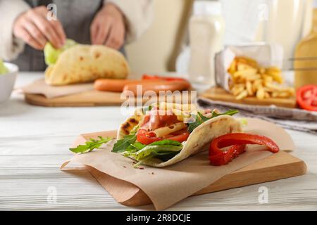 Donna che cucina delizioso pita wrap con jamon, formaggio e verdure a tavola di legno. Focalizzare l'attenzione sul piatto Foto Stock