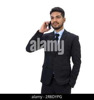Giovane uomo d'affari con baffi e barba vestita in abito nero con telefono cellulare mentre mette la mano in pantaloni tasche. Verticale su sfondo bianco Foto Stock