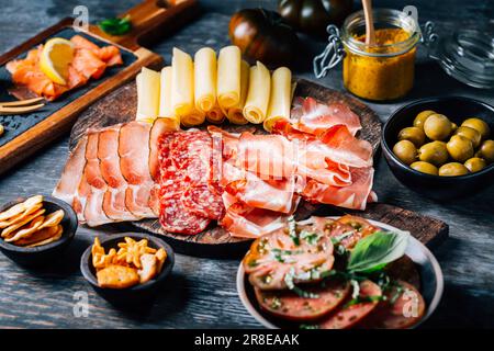 Antipasti con diversi antipasti, salumi, spuntini, piatto di carne con formaggio e olive speziate, carpaccio di salmone e insalata di pomodoro Foto Stock